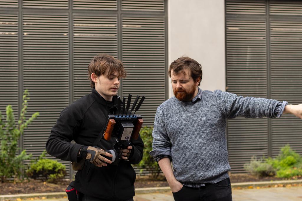 Charlie Hedger is holding a wireless video monitor and focus handset. He is talking to the Director who stands next to him.