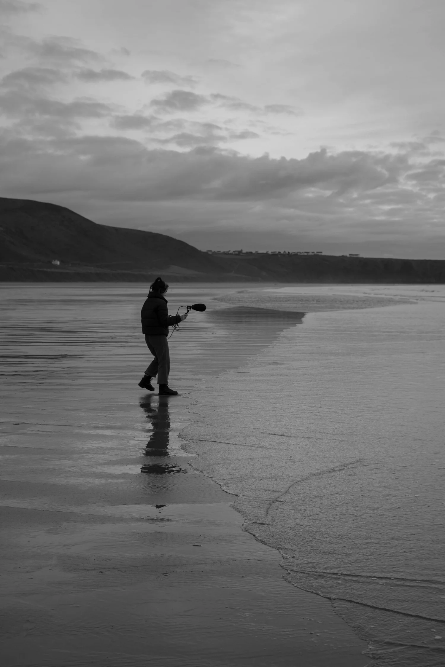 A black and white image of a sound operator recording sounds on a beach.