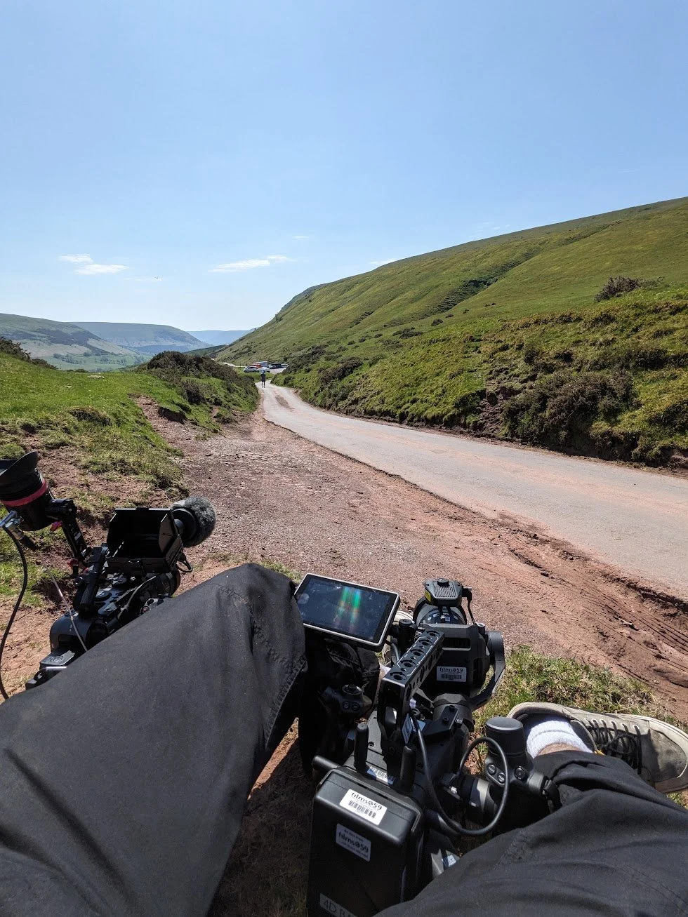 POV shot of Charlie Hedger at the top of a hill waiting for a cyclist. In front of him are two cinema cameras.
