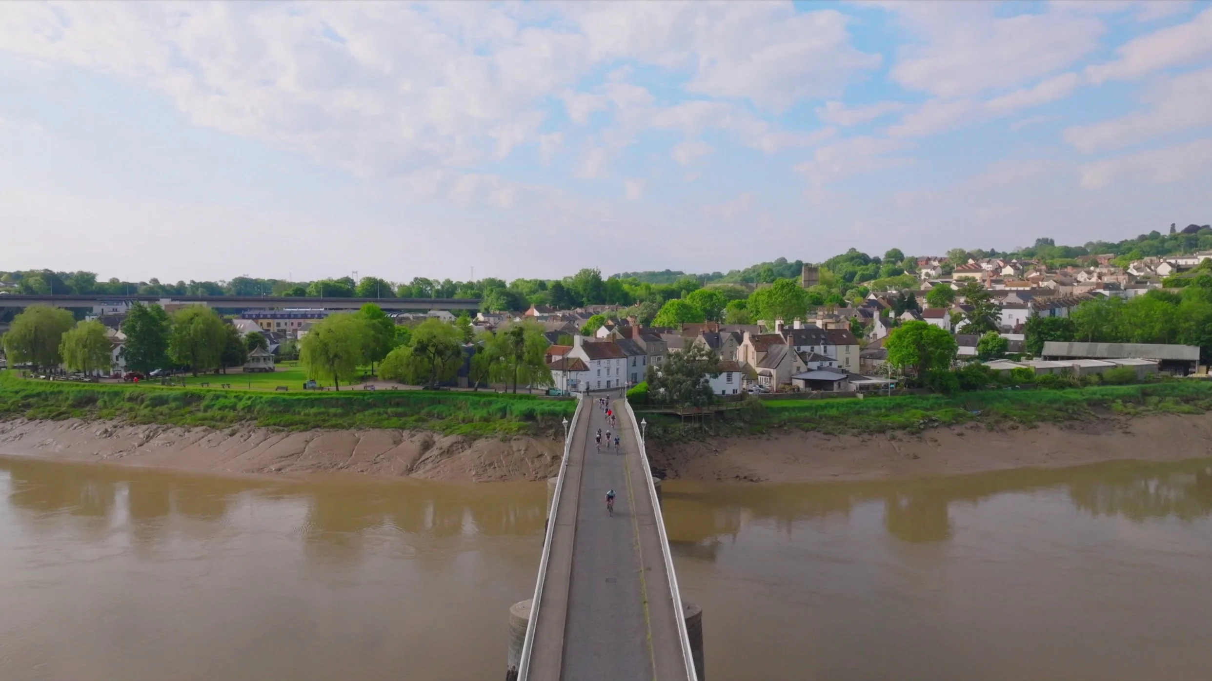 Aerial Drone Shot of a bridge with a group of cyclists racing across it.