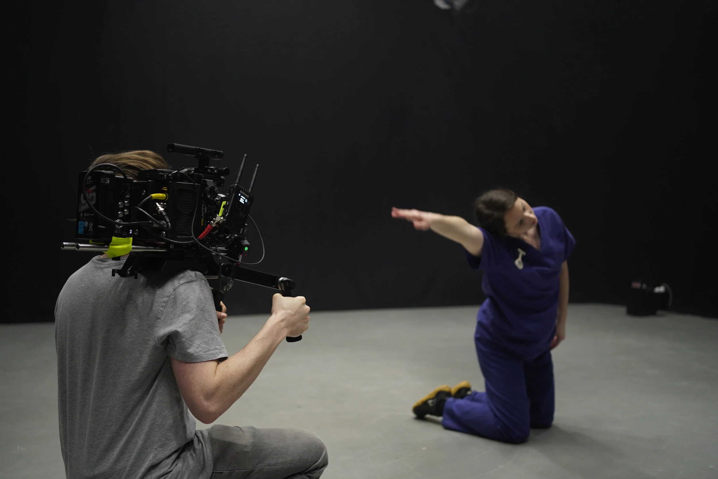 Charlie Hedger is crouched on a studio floor holidng a Cinema Camera.