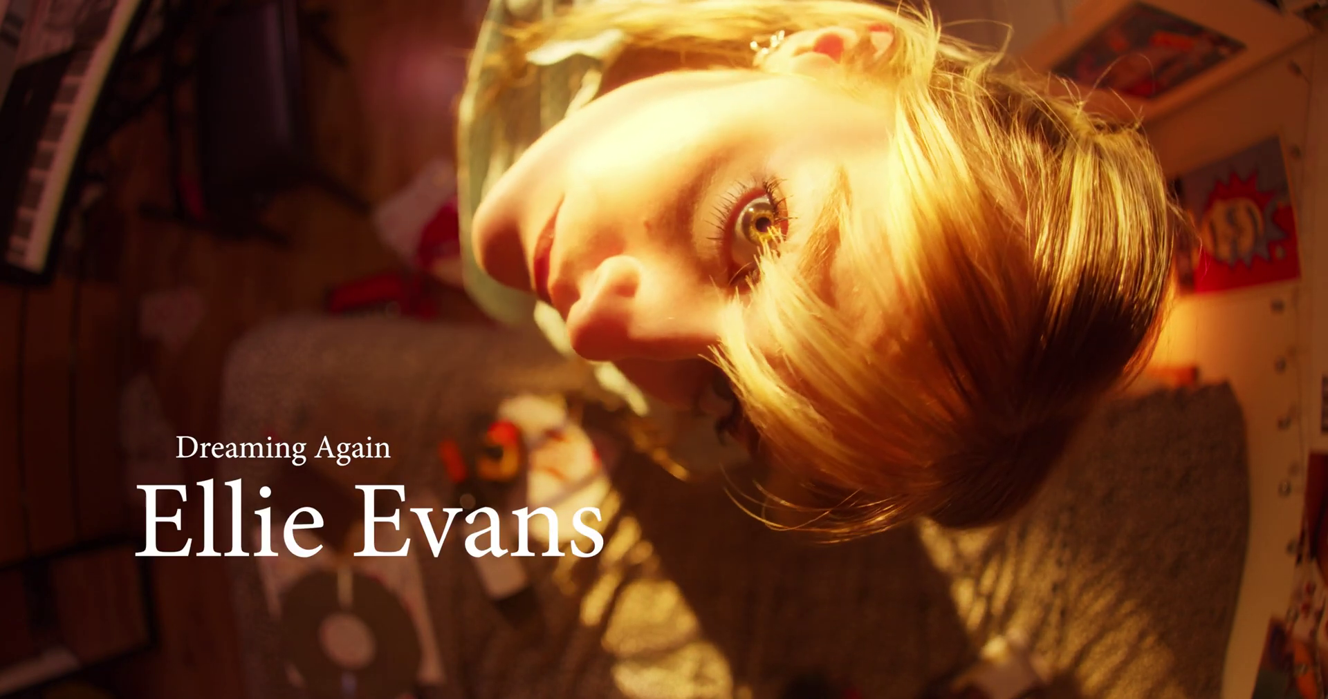 A close-up of a girl's face. She is looking down the lens of the camera. She is lit by a warm glow.