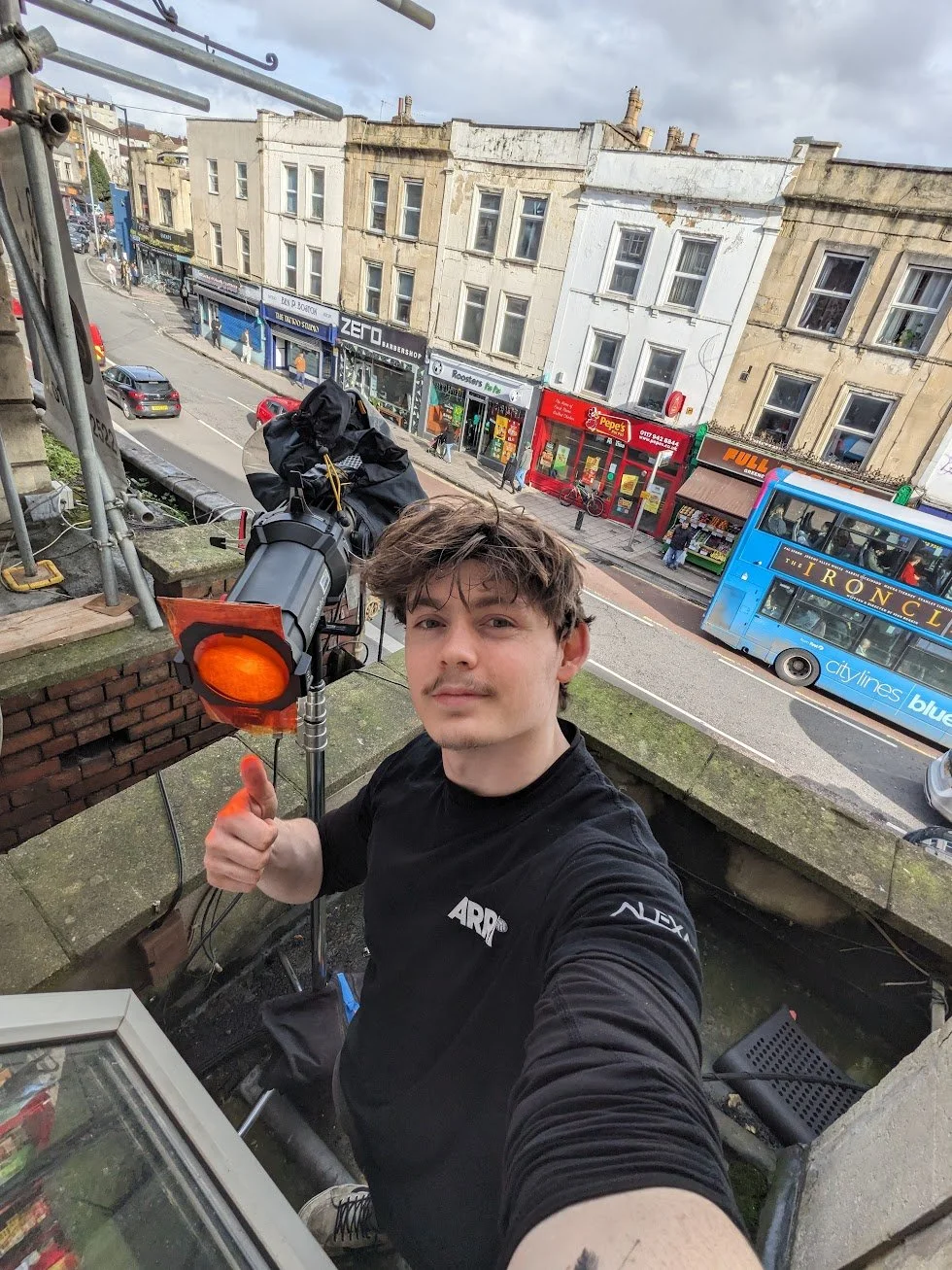 A self-taken picture of Charlie Hedger on a balcony with a Studio Light shining warm light through a window in front of him.