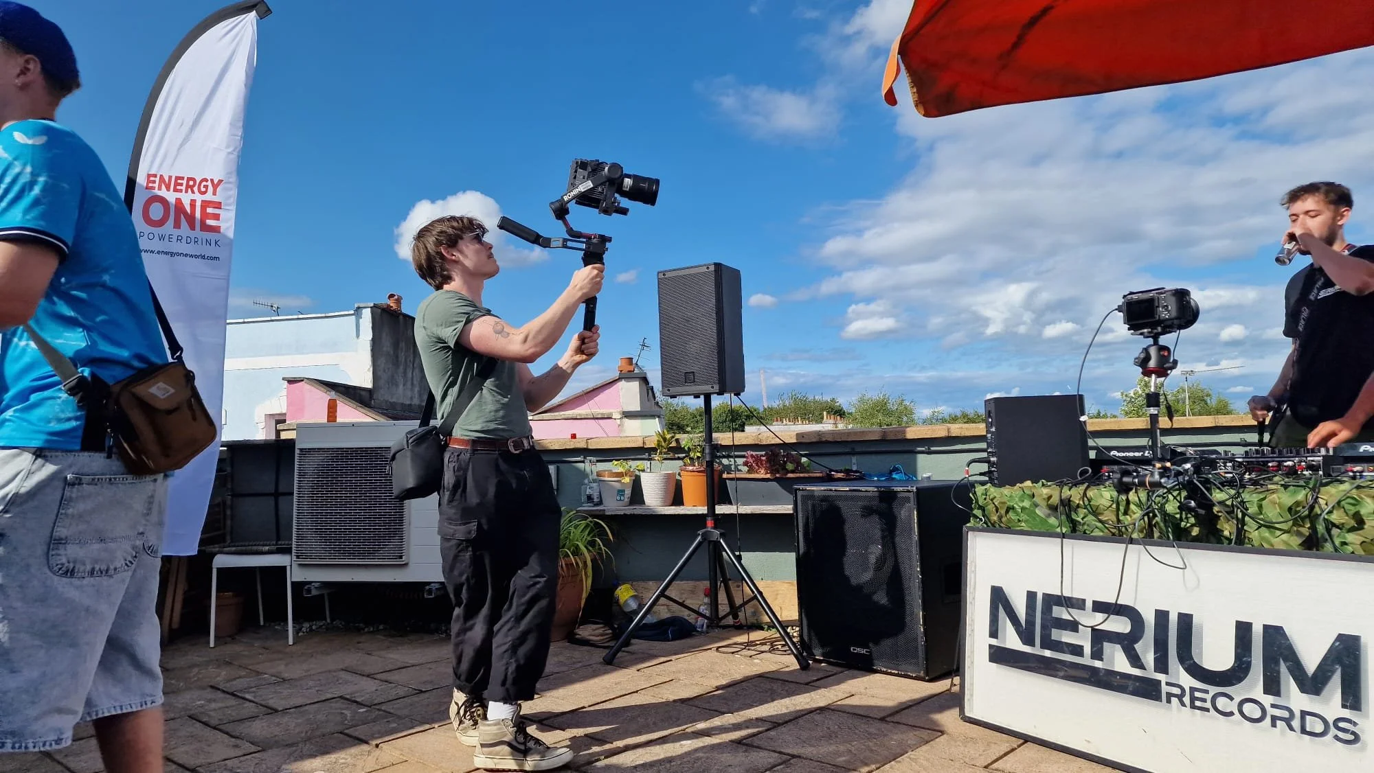 Charlie Hedger holding a cinema camera on a rooftop. It's a sunny day and he's pointing the camera at some DJ Decks.