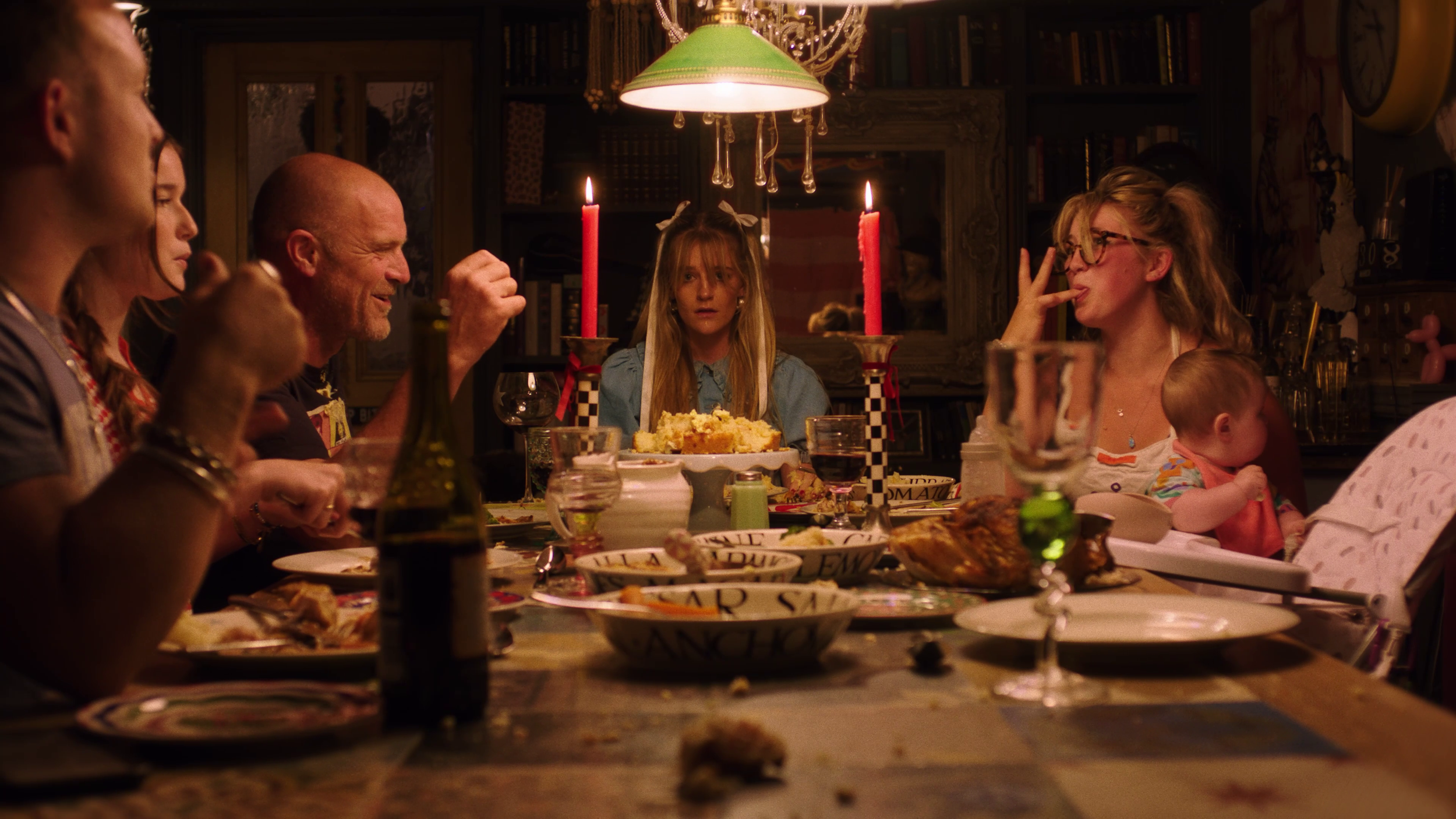 Ellie Evans sat at the end of a dining table. She is looking into the camera and is sat in front of a destroyed birthday cake.