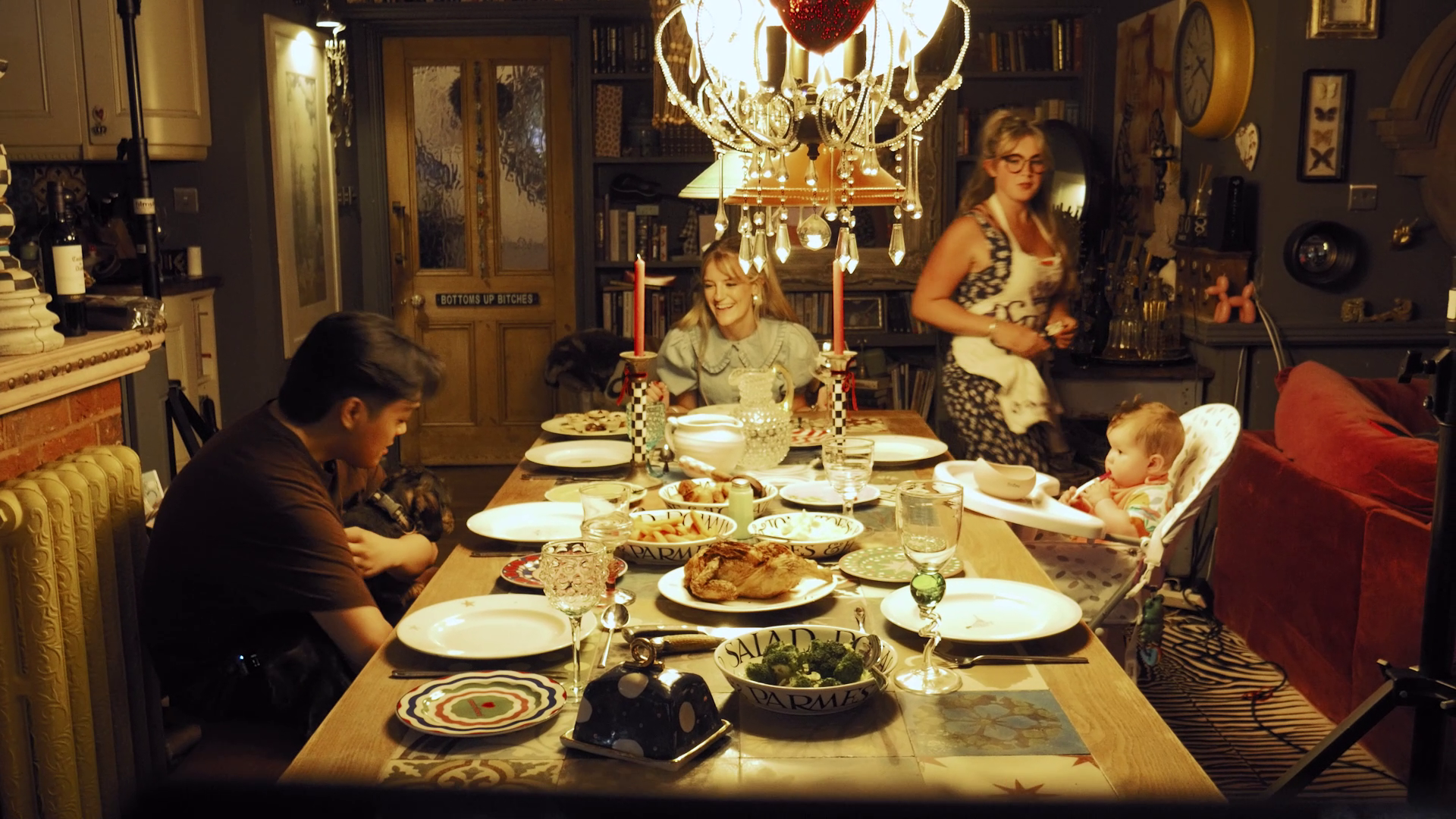Ellie Evans sat at the end of a dining table. She is smiling. There is a roast chicken on the table.