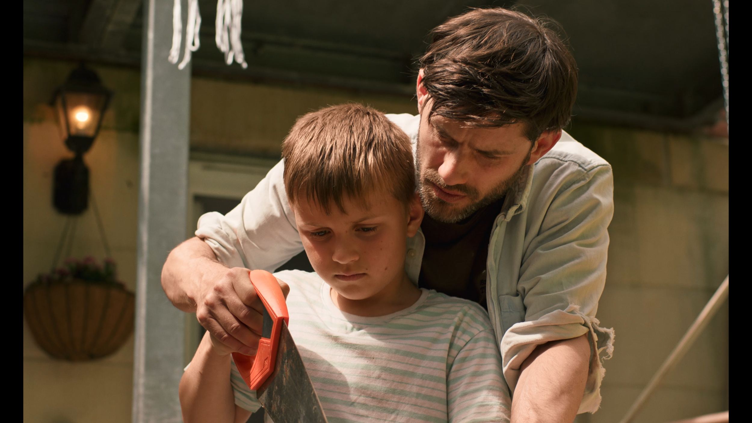 A father is guiding his son on how to use a wood saw. They are both gripping the handle.